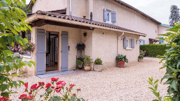 A two-story house with a gravel driveway, potted plants, and a door leading to the interior.