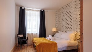 A bedroom with a bed, a chair, a bedside table, and a window with curtains.