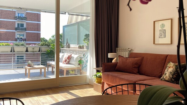Ein modernes Wohnzimmer mit einer Schiebeglastür zum Balkon, einem braunen Sofa, einem kleinen Tisch und einer Topfpflanze.