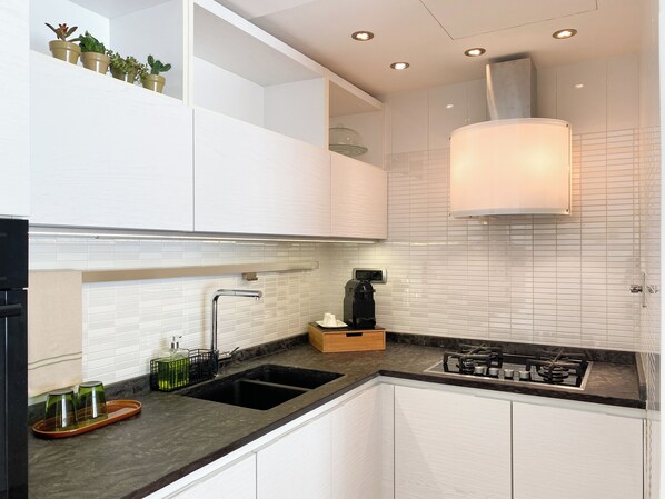 A modern kitchen with white cabinets, a black countertop, a built-in stove, and a coffee maker. - Be Close - Porta Portese Apartment with Terrace Near Trastevere (Roma)
