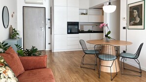 Eine moderne Küche mit weißen Schränken, einem eingebauten Ofen und einem Essbereich mit rundem Tisch und Drahtstühlen.