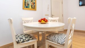 Un coin repas avec une table ronde, quatre chaises blanches, un saladier de fruits et un tableau accroché au mur.
