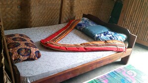 A wooden bed with a floral mattress cover, a red and yellow striped pillow, and a blue pillow with a floral pattern.