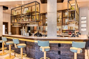 A bar area with a counter, stools, and shelves with bottles and glasses.