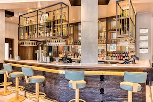 A bar area with a counter, stools, and shelves with bottles and glasses.