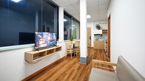 Una habitación moderna con un ventanal grande, televisor de pantalla plana, suelo de madera, zona de comedor y kitchenette.