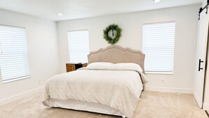 A bedroom with a bed, two windows with blinds, a wooden nightstand, and a door. - Cozy Country Farmhouse (Burley)