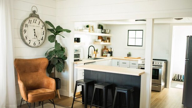 A modern kitchen with white cabinetry, a wooden island, black bar stools, and a vintage clock. - Cozy Country Farmhouse (Burley)