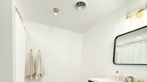 A bathroom with a white shower, a black vanity with gold handles, and a white sink. - Cozy Country Farmhouse (Burley)