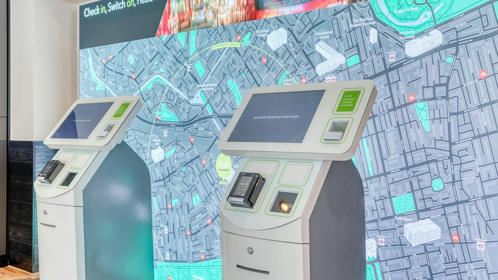 Two self-service kiosks with a digital map display in the background.