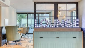 Een zithoek met een 'LOUNGE' bord, houten meubels en uitzicht door grote ramen.