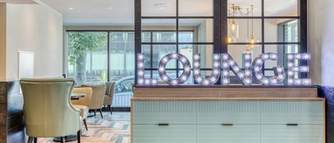 A lounge area with a 'LOUNGE' sign, wooden furniture, and a view through large windows.