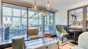 Een moderne hotel lobby met lederen zitplaatsen, een glazen wand met uitzicht op geparkeerde scooters, en een houten tafel.