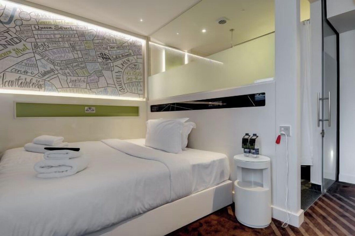 Una moderna camera d'albergo con un letto rifatto, una mappa appesa al muro e un piccolo comodino con articoli da toilette.
