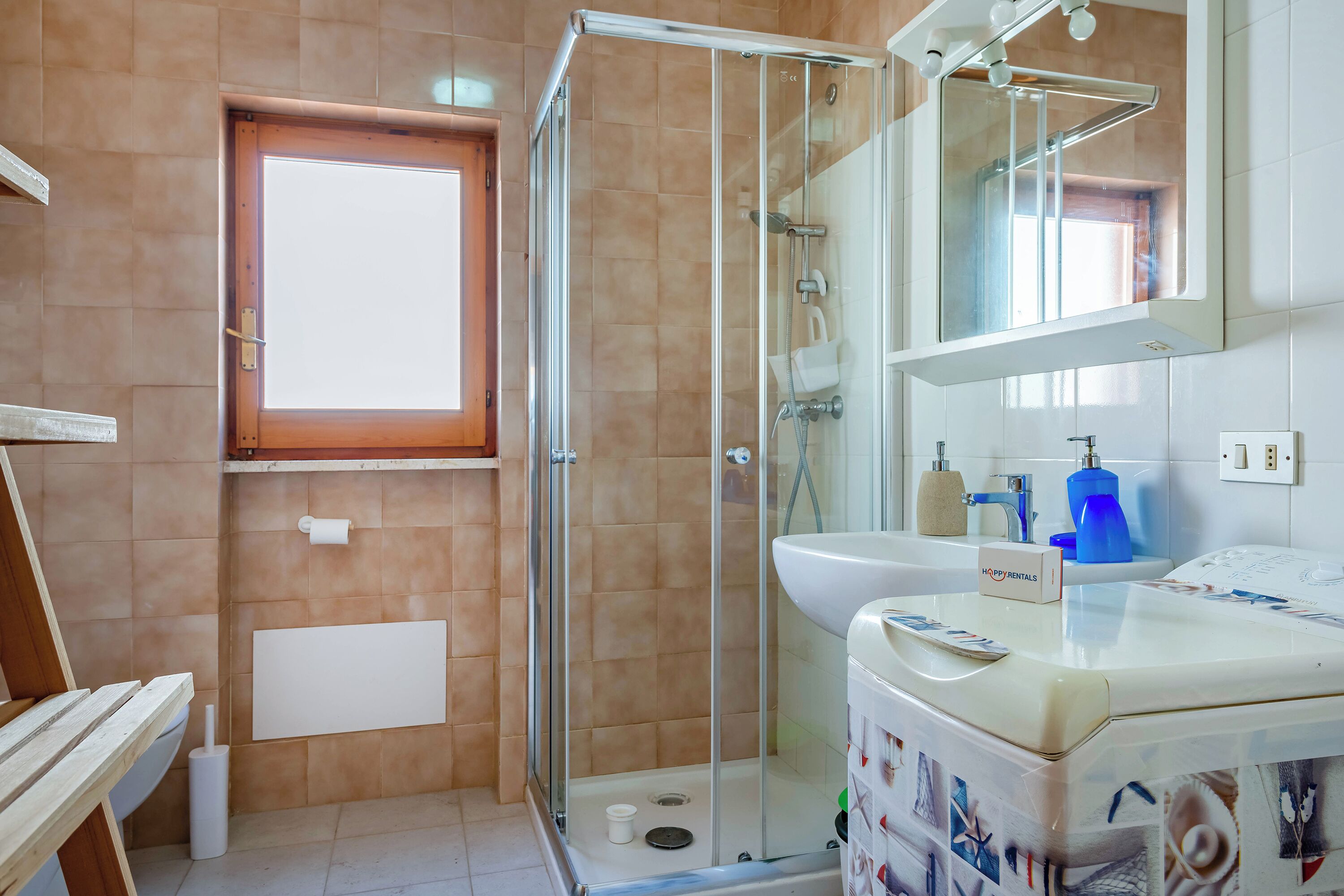 A bathroom with a glass shower enclosure, a sink with a mirror above it, and a window providing natural light.