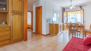 A spacious kitchen with wooden cabinets, a dining area with a table and chairs, and a red bed in the foreground. - Gelsi Mori Seafront Otranto (Otranto)