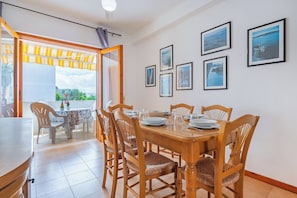 A dining area with a wooden table set for six, surrounded by wicker chairs. There are four framed pictures on the wall.