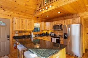 Ein Interieur einer Holzhütte mit einer Küche, die eine Granitarbeitsplatte, Edelstahlgeräte und Holzausstattung zeigt.