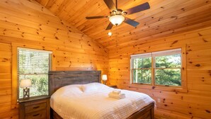 Une chambre dans une cabane en bois, avec un lit, des tables de chevet, un ventilateur de plafond et des fenêtres.