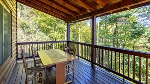 Une terrasse en bois avec une table et des chaises, donnant sur une zone boisée.