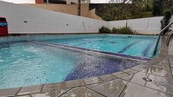 A swimming pool with clear water, a tiled deck, and a metal handrail.