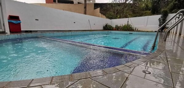 A swimming pool with clear water, a tiled deck, and a metal handrail.