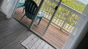 Une pièce dotée d’une porte-fenêtre coulissante donnant sur un balcon avec vue sur l’océan et la végétation.