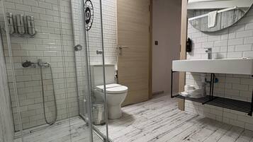 Un baño con cabina de ducha de vidrio, inodoro y lavamanos con toallero.