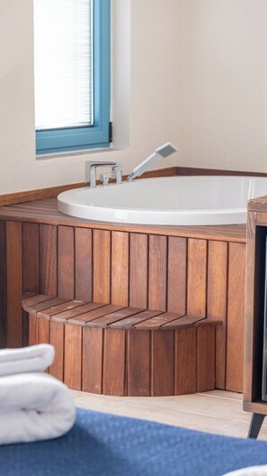 A wooden bathtub with a built-in showerhead, a window with blinds, and a towel on the floor. - Cunda Nisa Otel (Ayvalik)