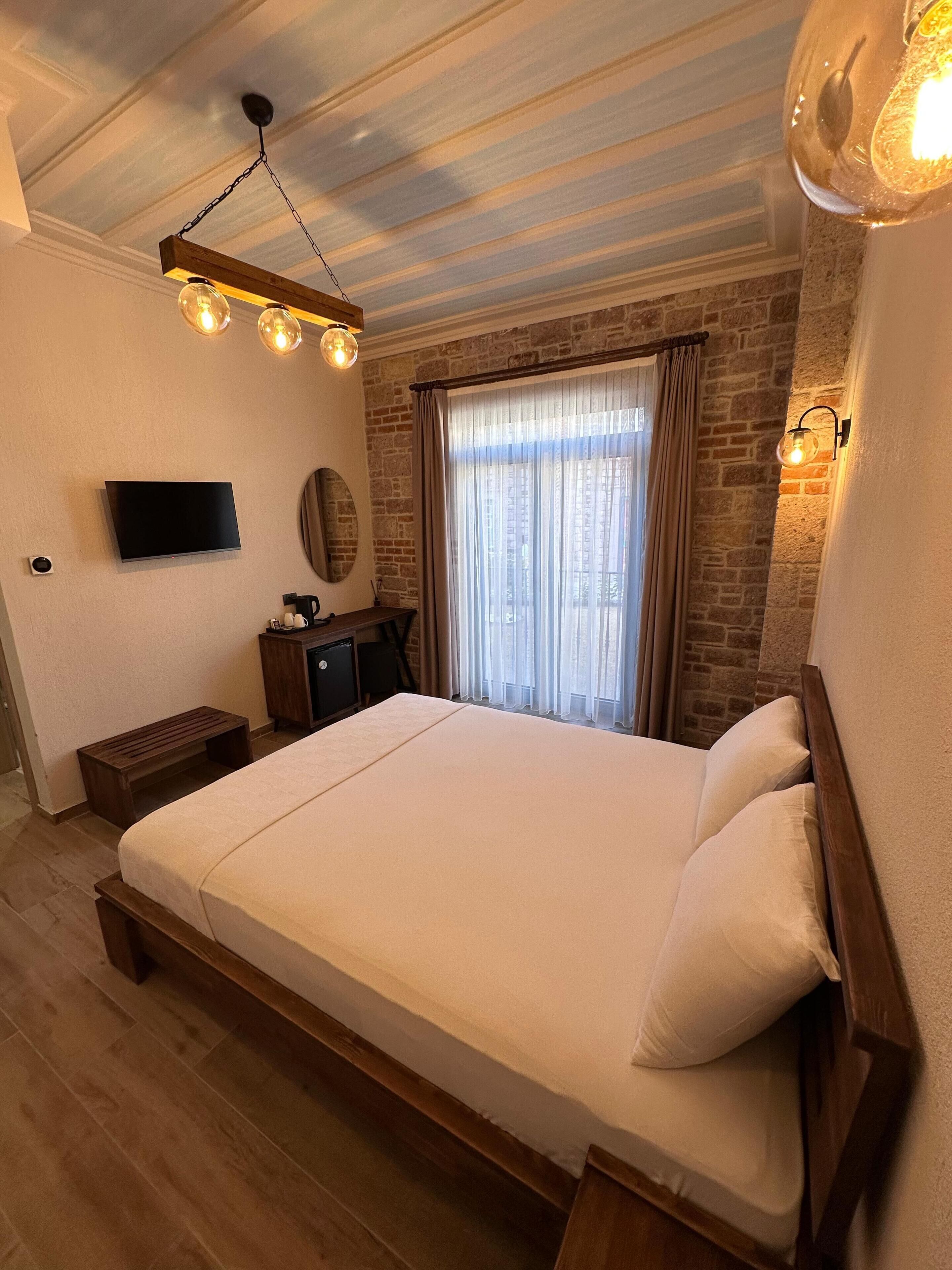 Quarto com cama de madeira, televisão de tela plana, pequena escrivaninha e parede de tijolos.