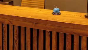 A reception desk with a wooden finish and a blue bell on it. Above the desk, there is a wall-mounted sign with illuminated letters spelling "GUNDA NISA RECEPTION". - Cunda Nisa Otel (Ayvalik)