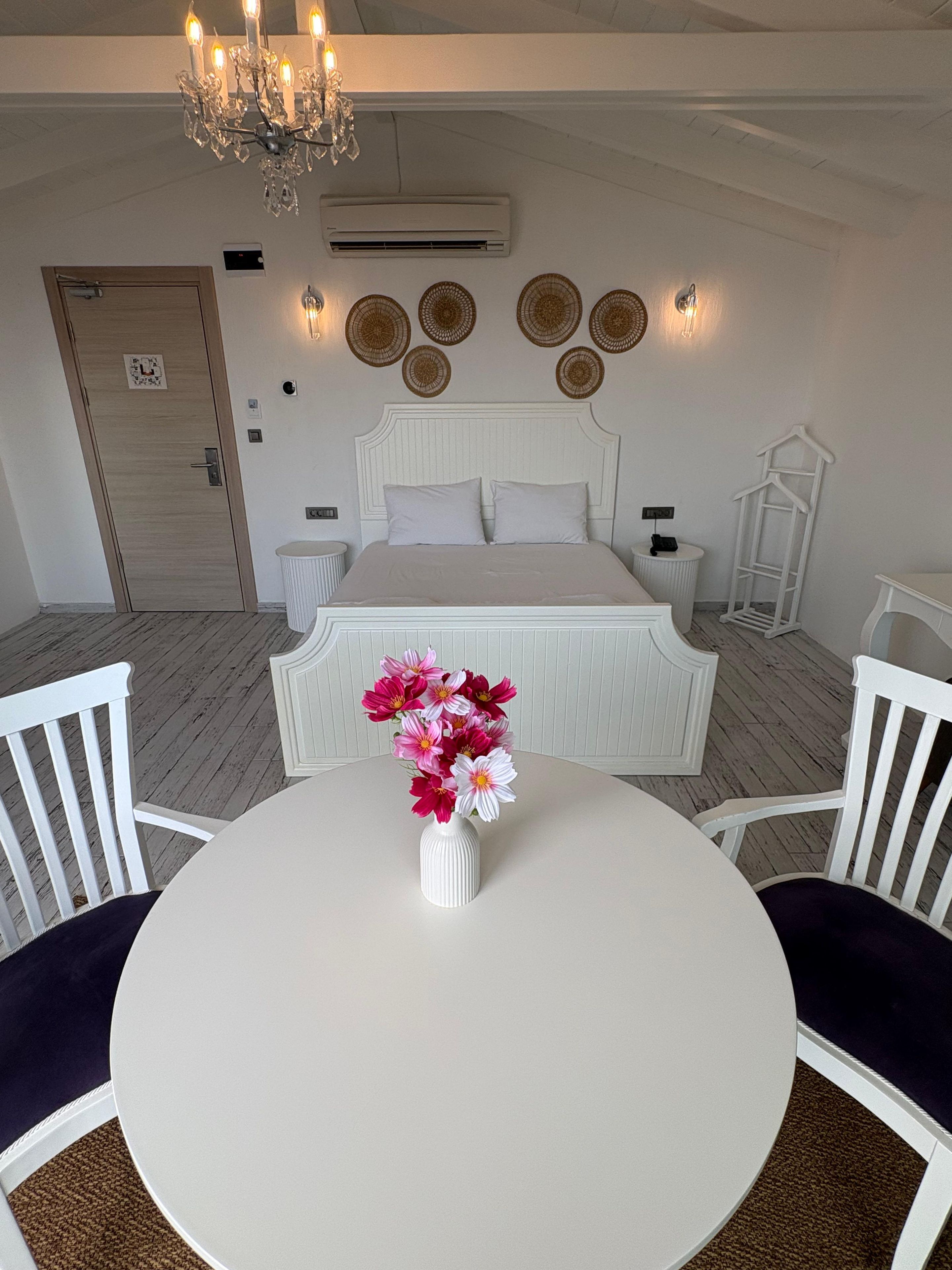 Un dormitorio con cama, mesitas de noche, una araña, decoración en la pared y una zona de comedor con mesa y sillas.