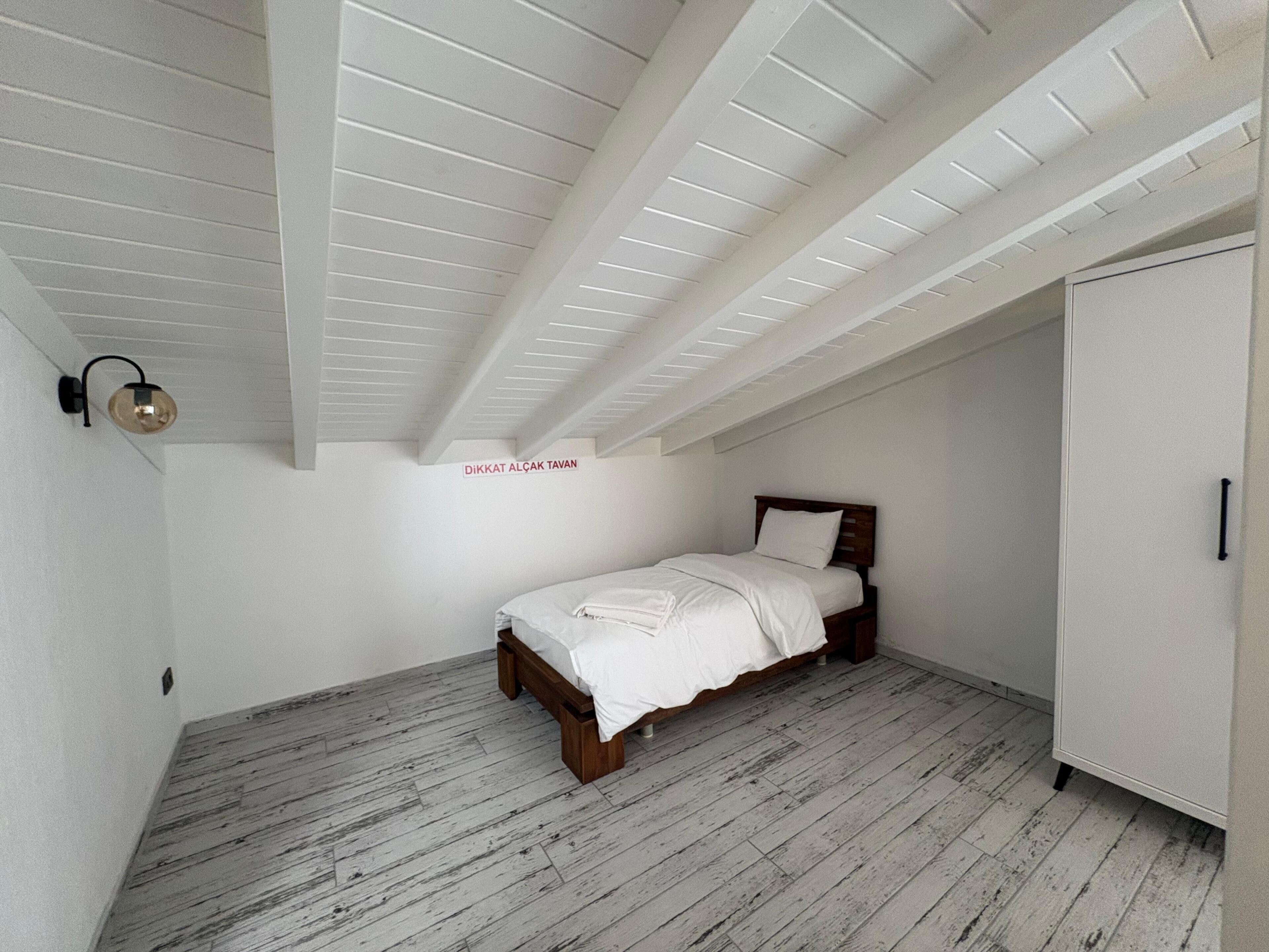 A bedroom with a sloped ceiling, a bed, a wardrobe, and a wall-mounted light fixture.