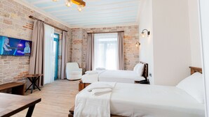 A hotel room with a brick wall, two beds, a TV, and a wooden bench. - Cunda Nisa Otel (Ayvalik)