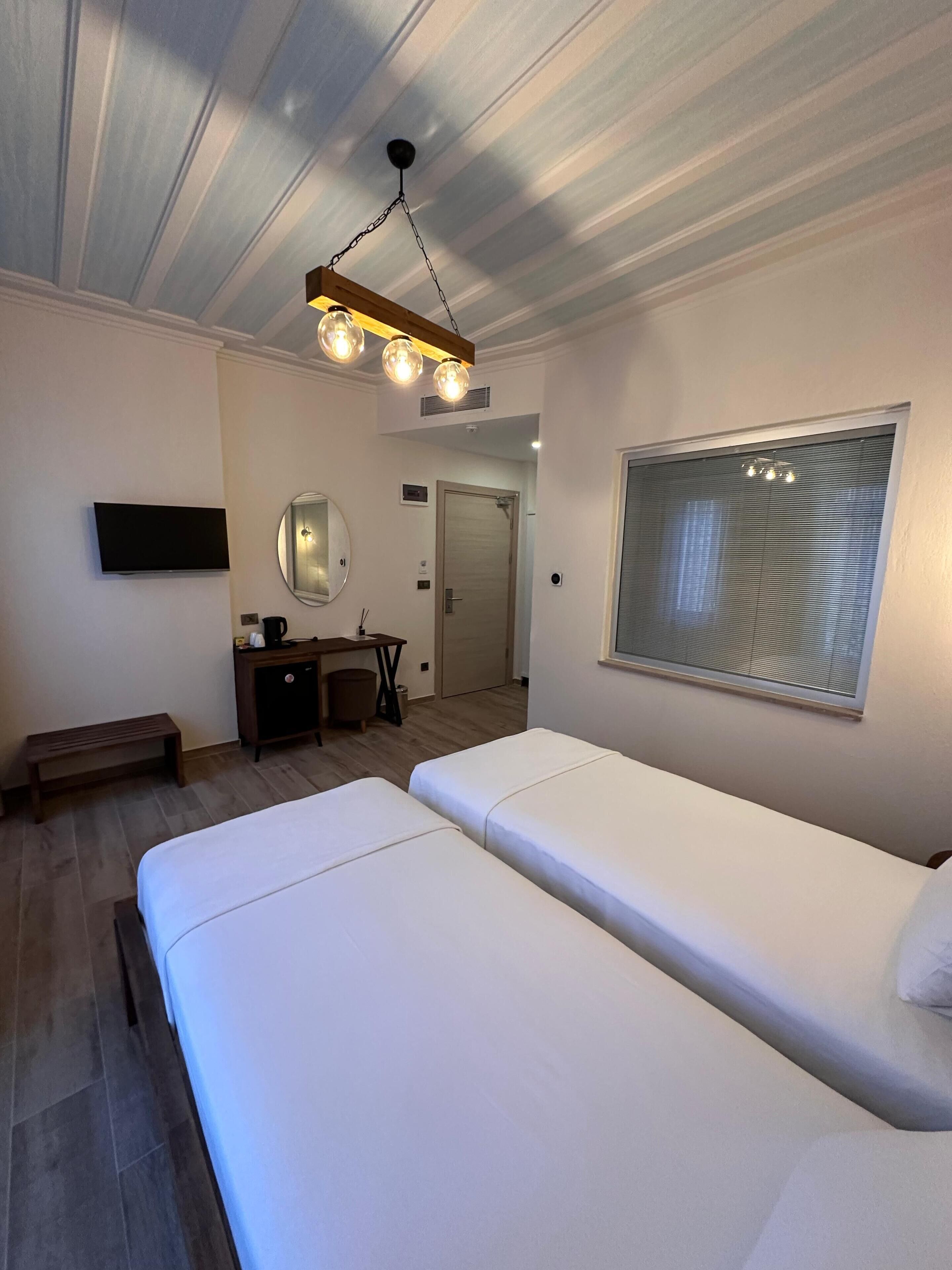 A hotel room with a large bed, a desk with a chair, a TV mounted on the wall, and a window with blinds.