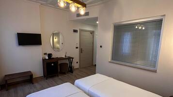 A hotel room with a large bed, a desk with a chair, a TV mounted on the wall, and a window with blinds.
