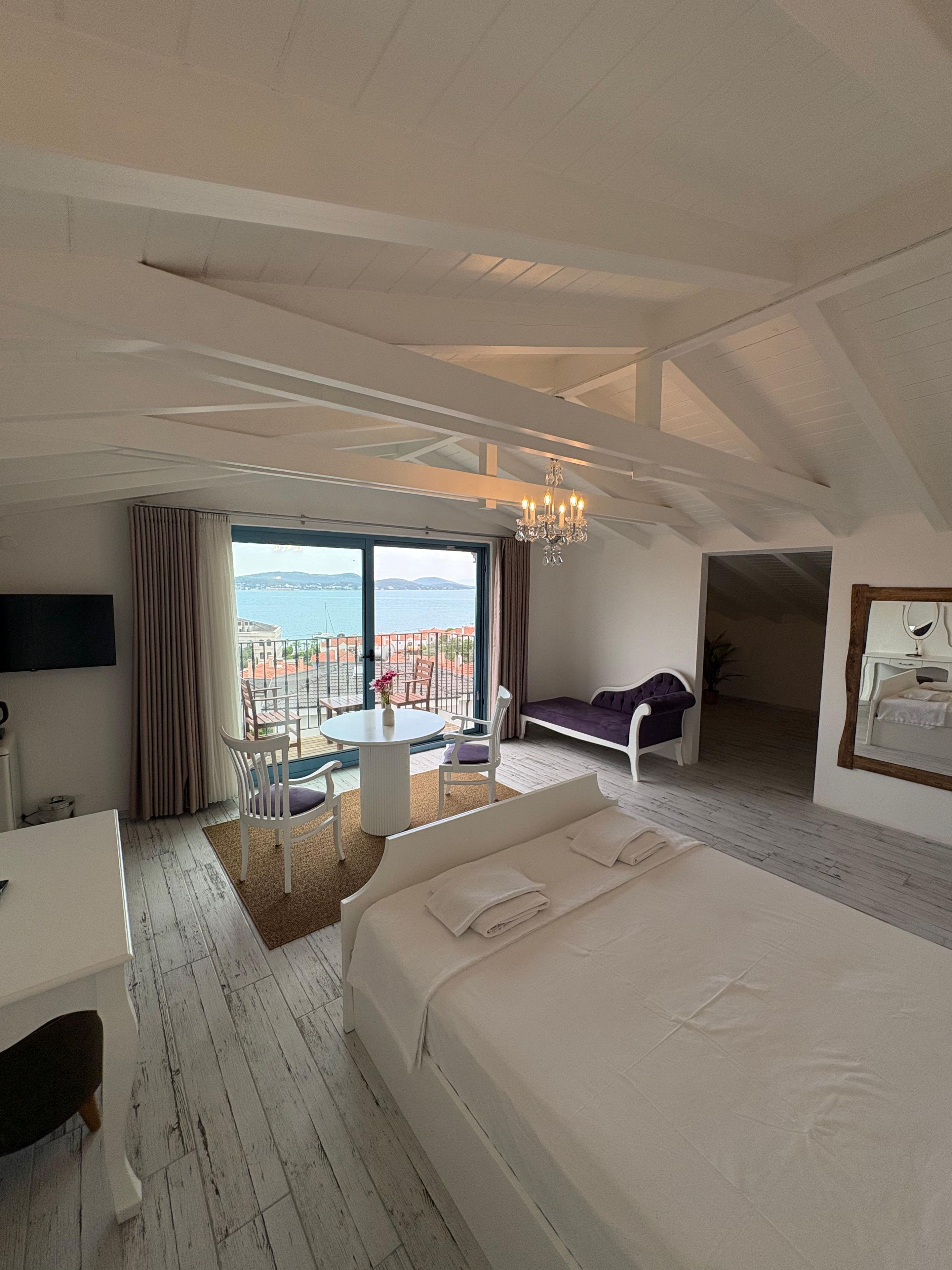 Quarto com cama grande, escrivaninha, cadeira, sofá e vista para o mar.