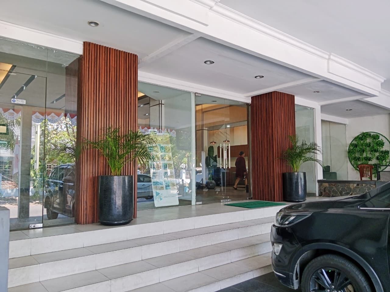 A hotel entrance with a glass facade, steps leading up to the door, and a black car parked in front.