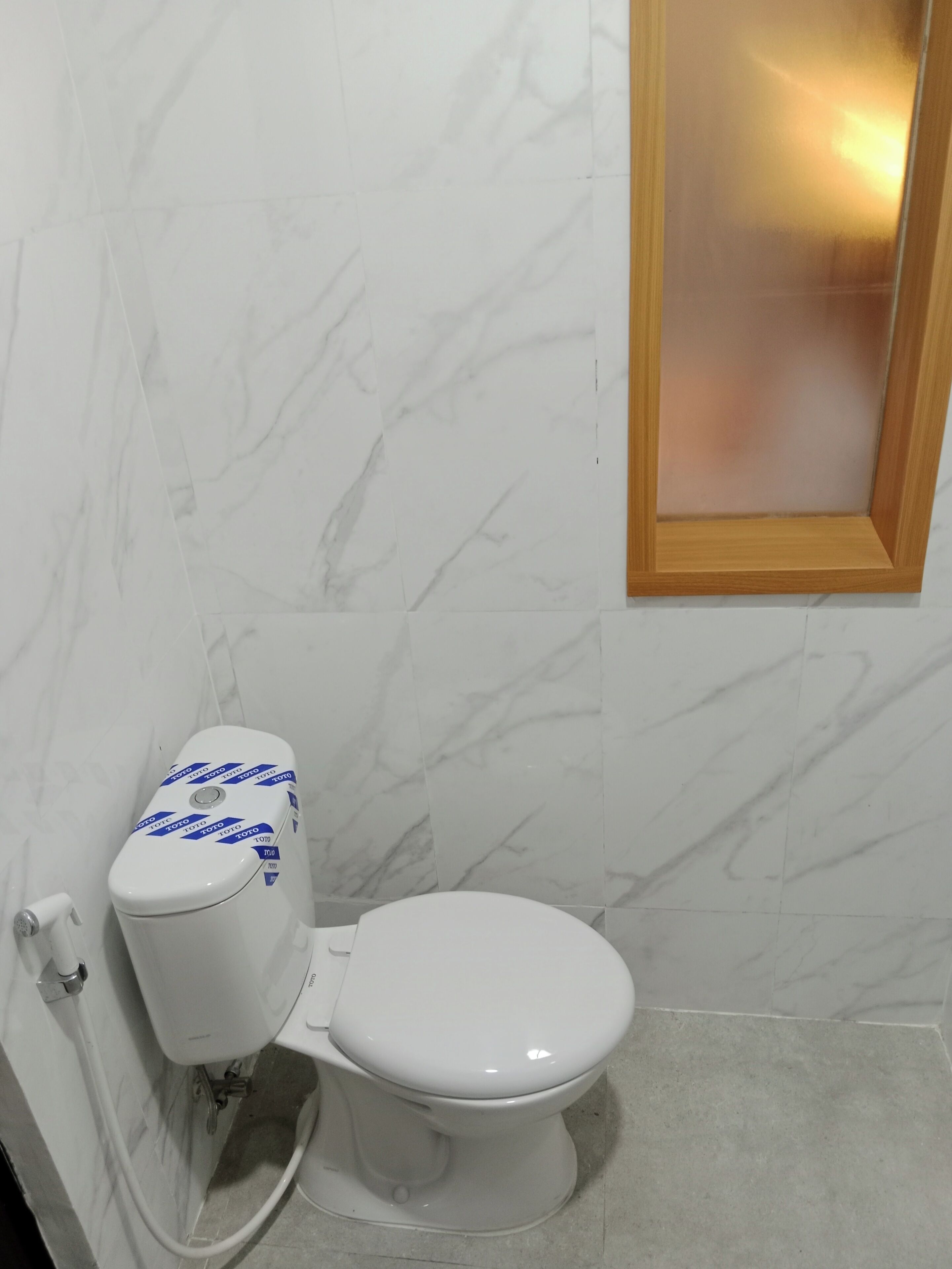 Eine weiße Toilette mit Wand in Marmoroptik und einem spiegelnden Wandbild an Holzrahmen.