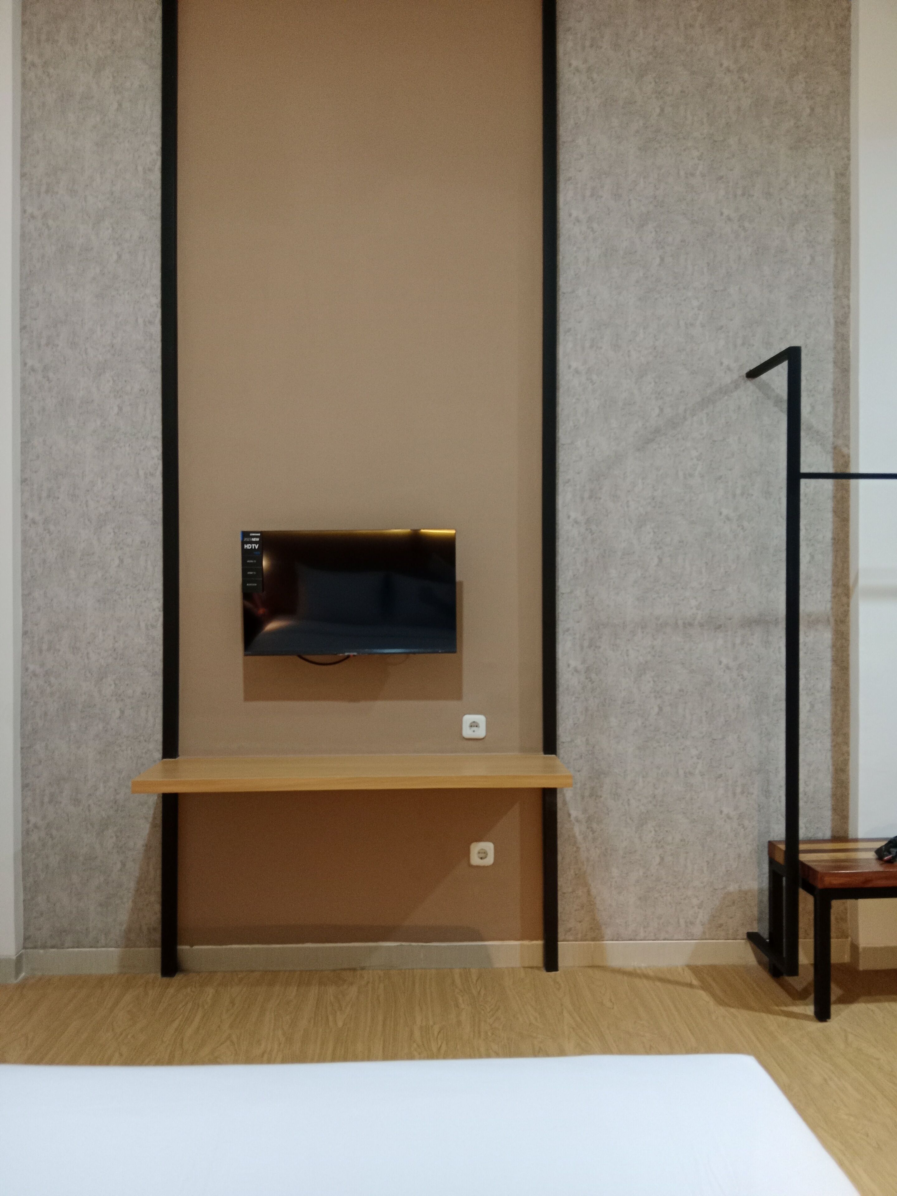 A room with a flat-screen TV mounted on a wall, a wooden bench, and a black metal stand.