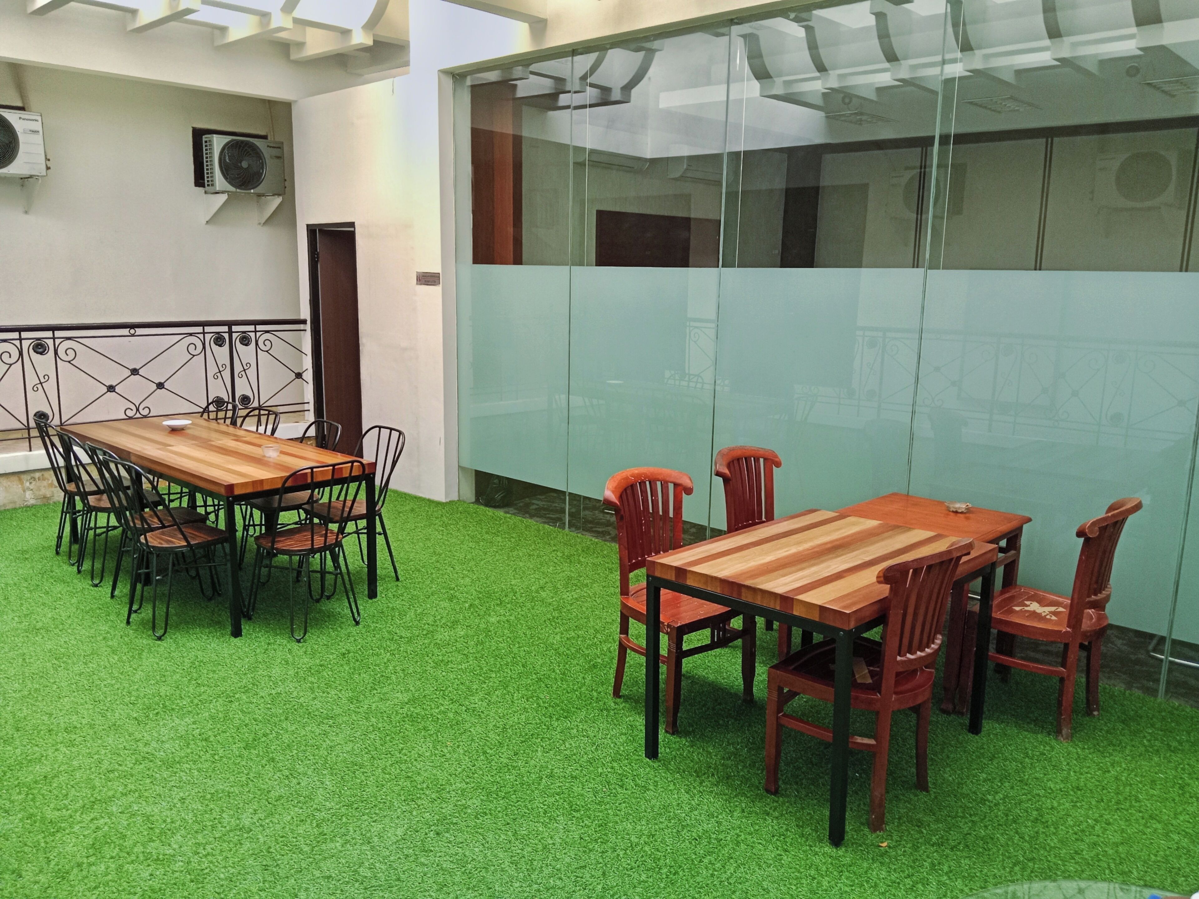 A conference room with a wooden table and chairs, green artificial grass flooring, and glass partitions.