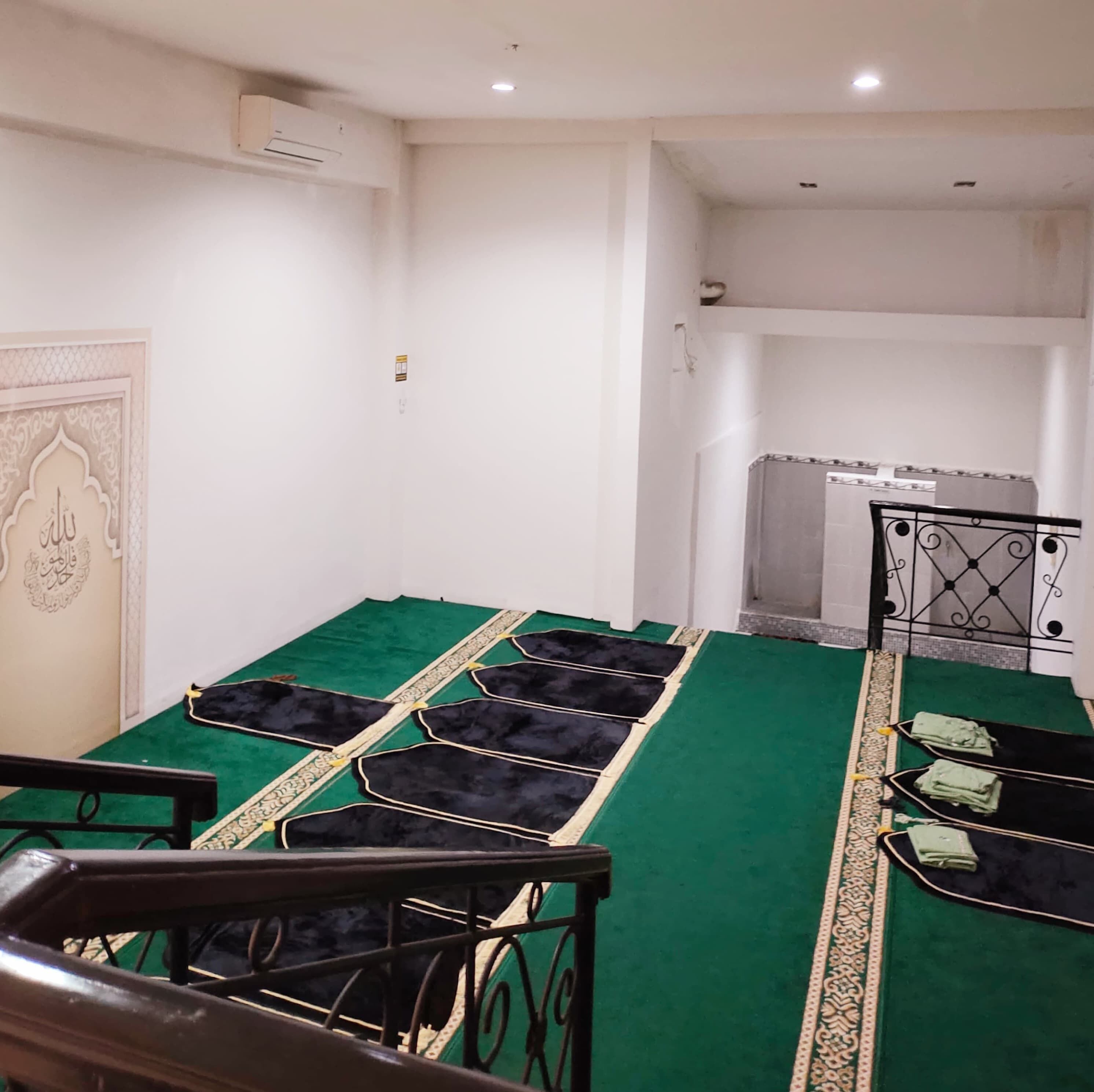 A prayer room with green carpeting, a prayer mat, and a small prayer niche.