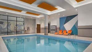 Une piscine intérieure à l’eau claire, dotée de chaises longues orange et d’un design moderne au niveau du plafond.