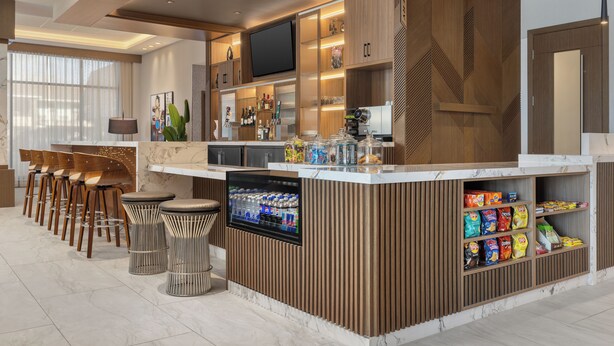 Un espace bar moderne doté d’un téléviseur à écran plat, de tabourets de bar et d’étagères remplies de collations.