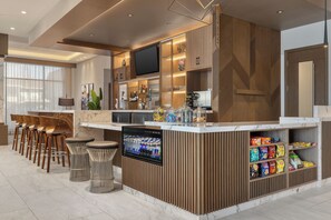 A modern bar area with a flat-screen TV, bar stools, and shelves stocked with snacks. - Hyatt Place Windsor (Windsor)