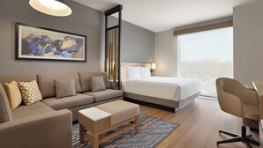 Une chambre d’hôtel moderne équipée d’un canapé, d’un lit, d’un bureau et d’une grande fenêtre donnant sur la ville.