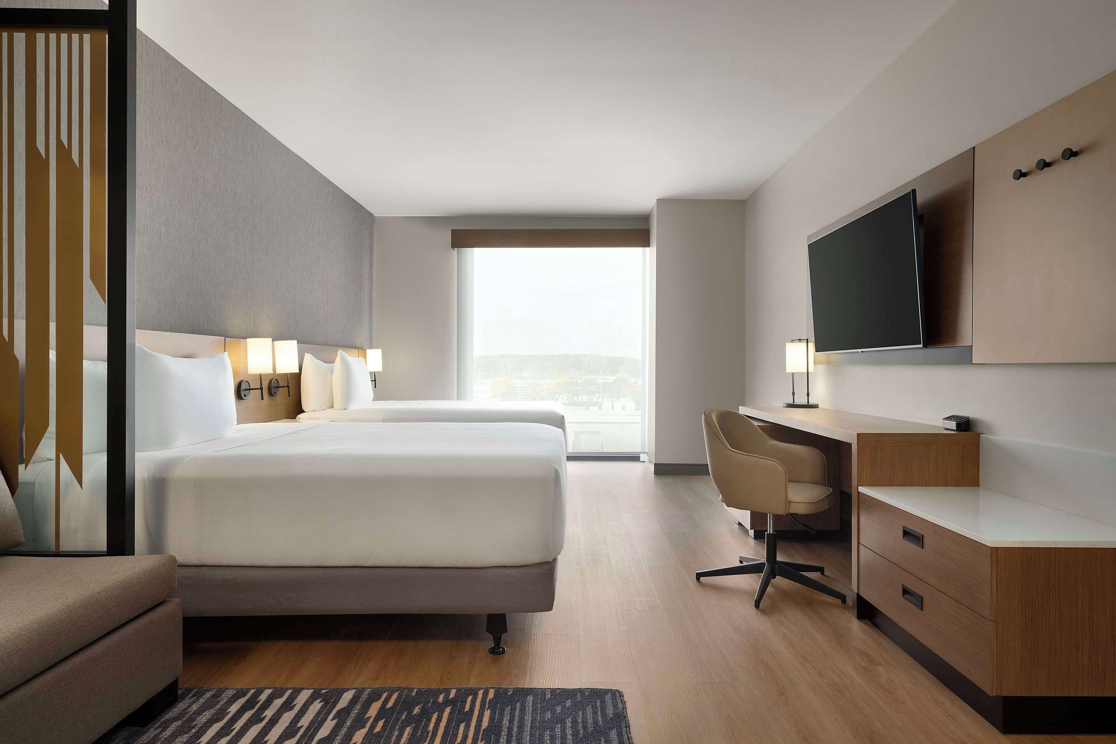 Habitación de hotel con una cama grande, un escritorio, un televisor y vistas a la ciudad.