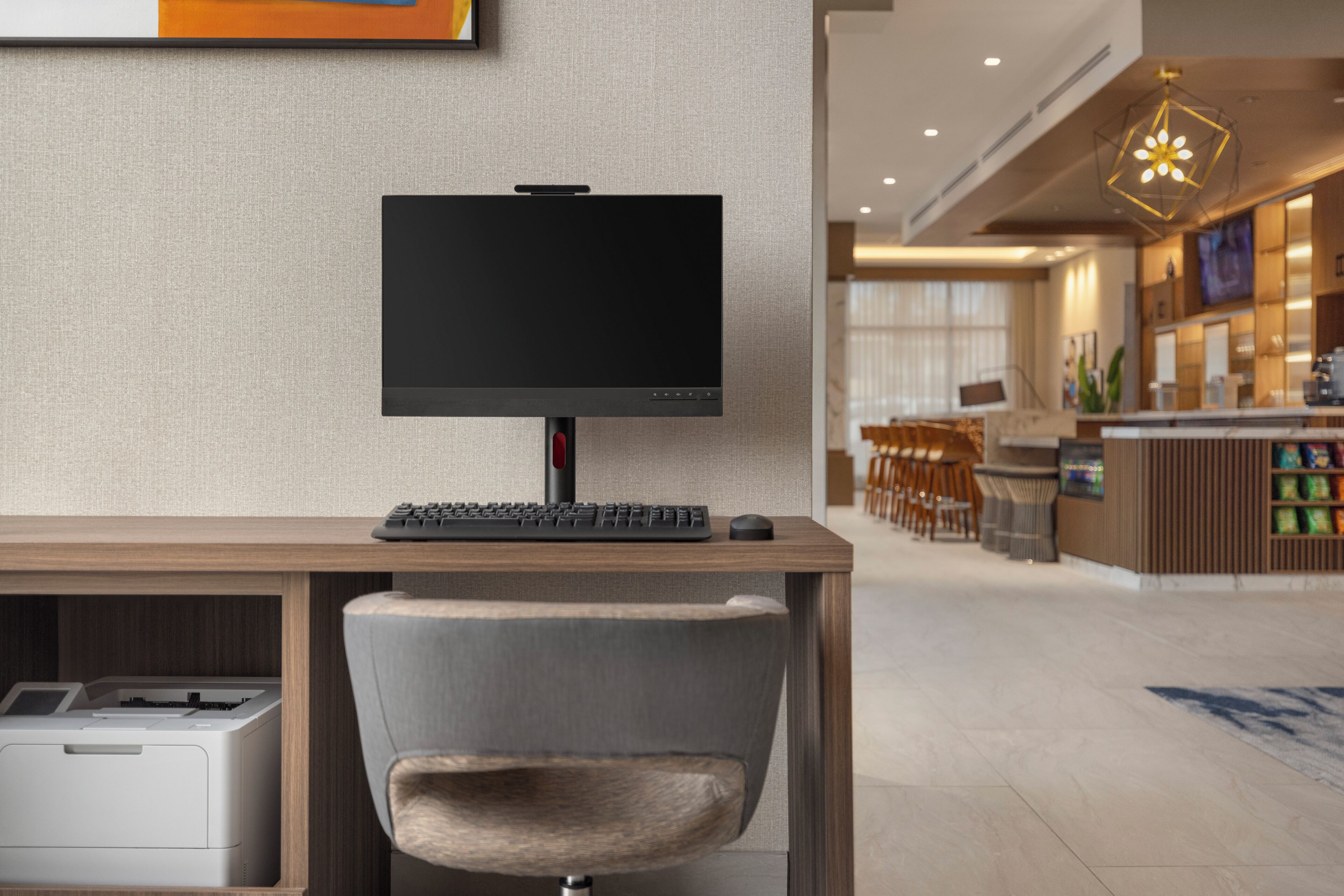 Un moderno vestíbulo de hotel con un mostrador de recepción de madera, un televisor de pantalla plana, un teclado, un ratón y una impresora.