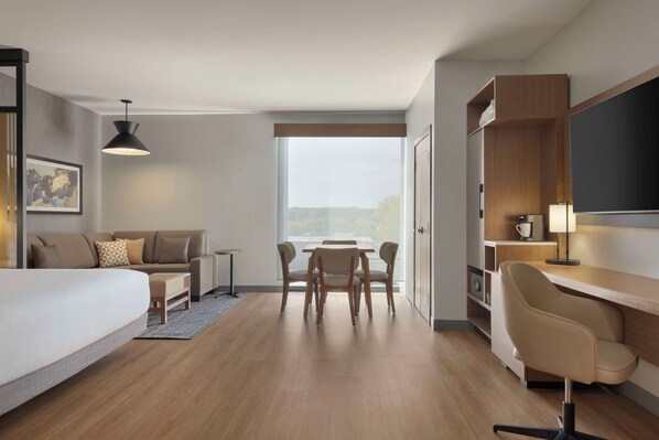Ein modernes Hotelzimmer mit einem Bett, einem Schreibtisch, einem Stuhl, einem Esstisch und einem großen Fenster.