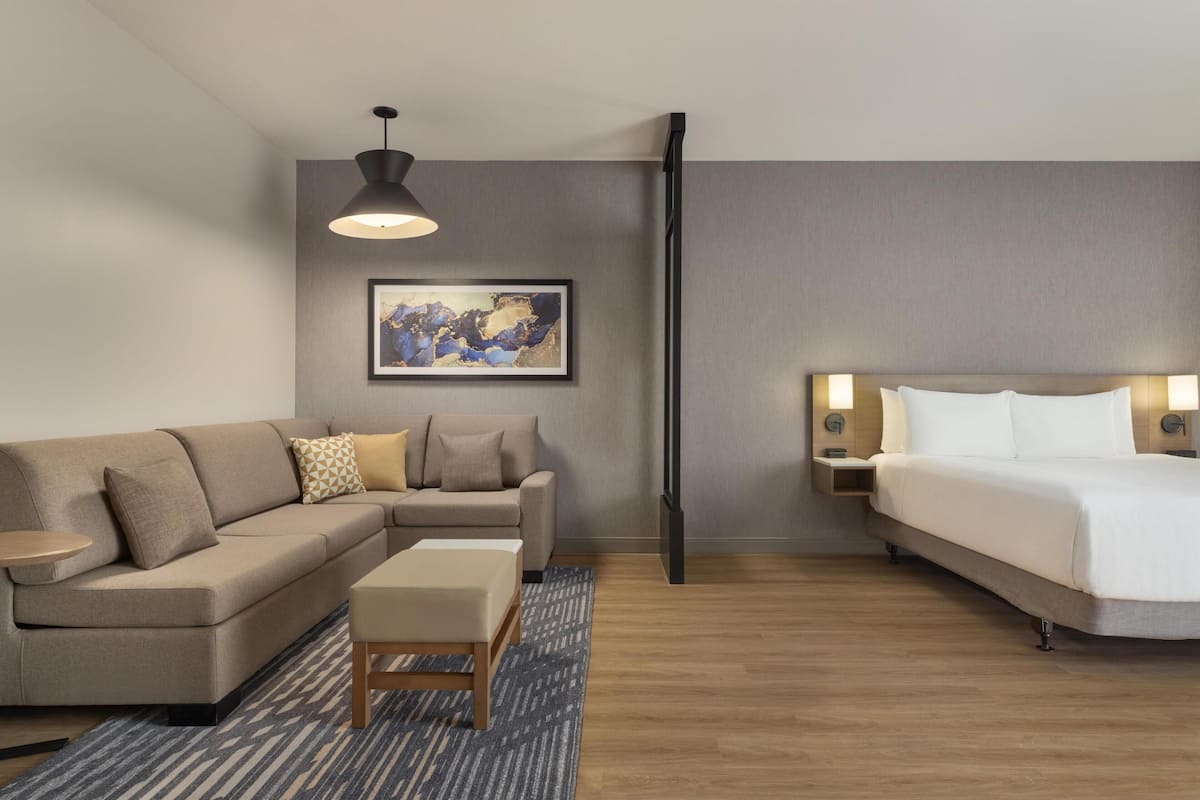 Ein modernes Hotelzimmer mit Sofa, Bett, kleinem Tisch und einem gerahmten Kunstwerk an der Wand.